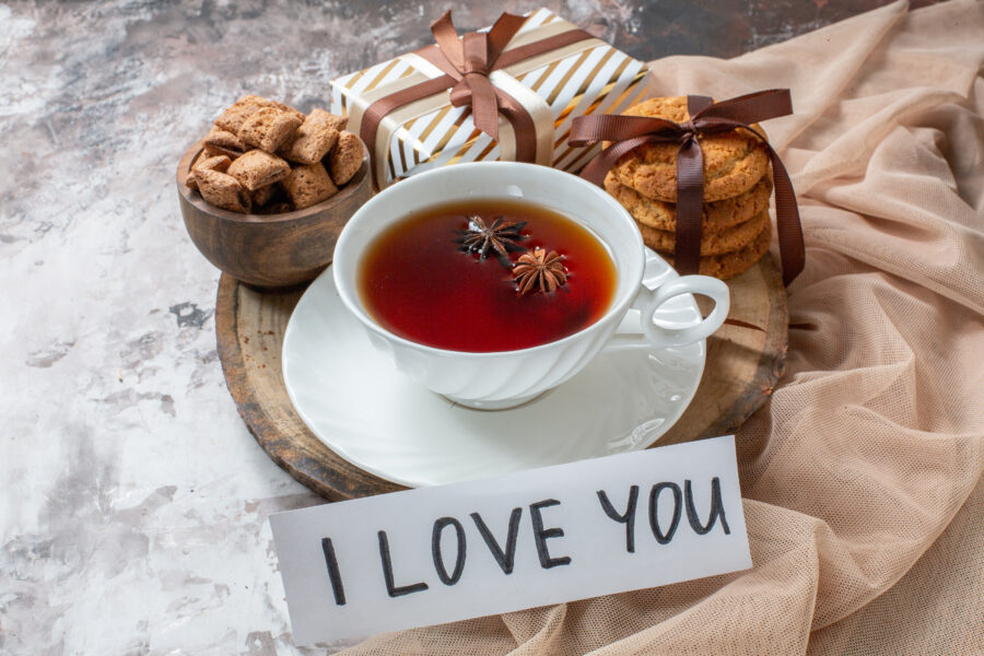 Luxurious Amorous Brew Ceylon black tea tin with rose petals and a teacup on a lace tablecloth in a romantic candlelit setting.